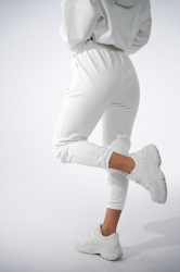 Brandenburg Couture DRES DAMSKI BG ROYAL SUEDE - biały - Komplet zamszowy BG ROYAL SUEDE w kolorze białym. Bluza kangurka z kapturem ozdobiona dużym haftowanym złotym logiem marki BG BRANDENBURG COUTURE. Spodnie posiadają gumkę w pasie. Na lewej kieszeni spodni wyhaftowane złote logo marki. Krój oversize. Ozdobne przeszycia na bluzie oraz spodniach.